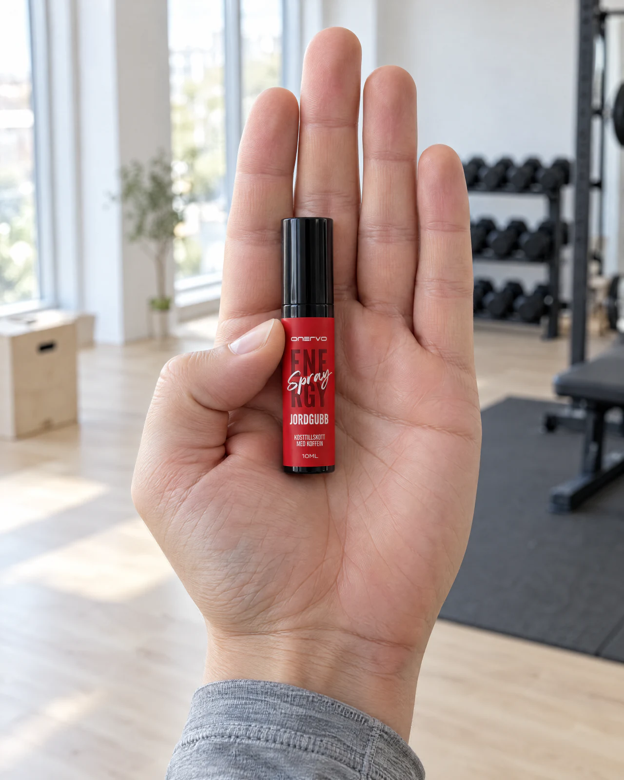 Otwarta dłoń trzyma Onervo Energy Spray Truskawka na siłowni.