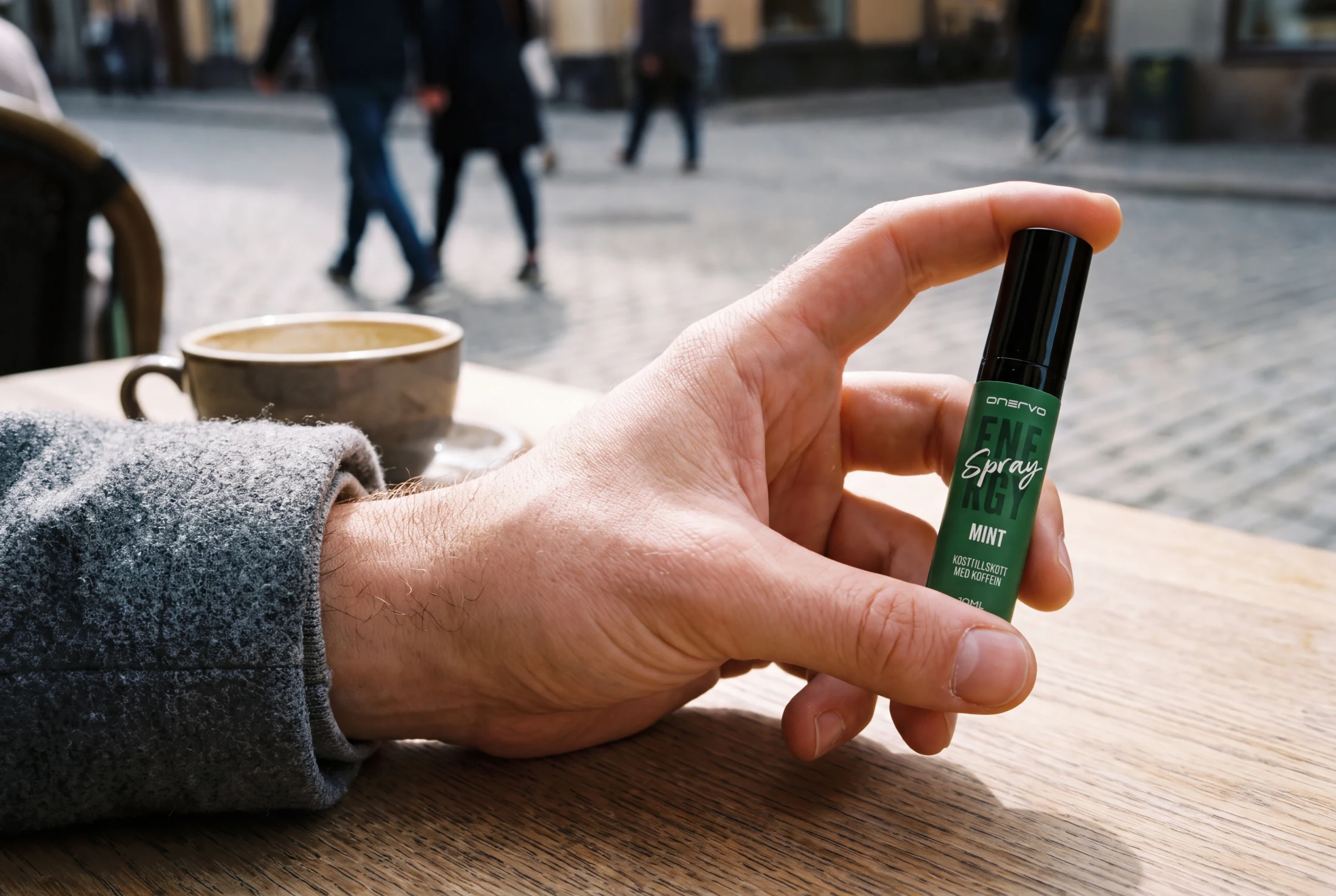 Dłoń trzyma Onervo Energy Spray Mięta przy stoliku w kawiarni na ulicy.